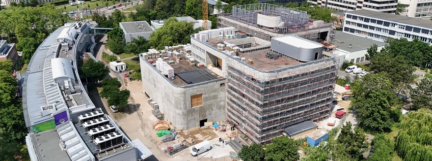 Construction of a new building for the MPI of Microstructure Physics Aerial perspective of a construction site featuring two prominent buildings, surrounded by scaffolding. Nearby roads and green trees are visible, indicating ongoing development.
