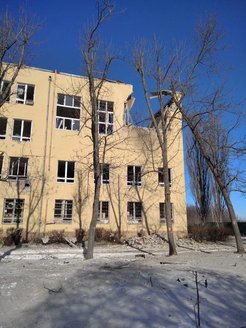 Hinter Bäumen ohne Blätter ist ein Gebäude mit fehlenden Fensterscheiben zu sehen, und in der oberen Ecke des Gebäudes fehlen die Decke und das gesamte Fenster.